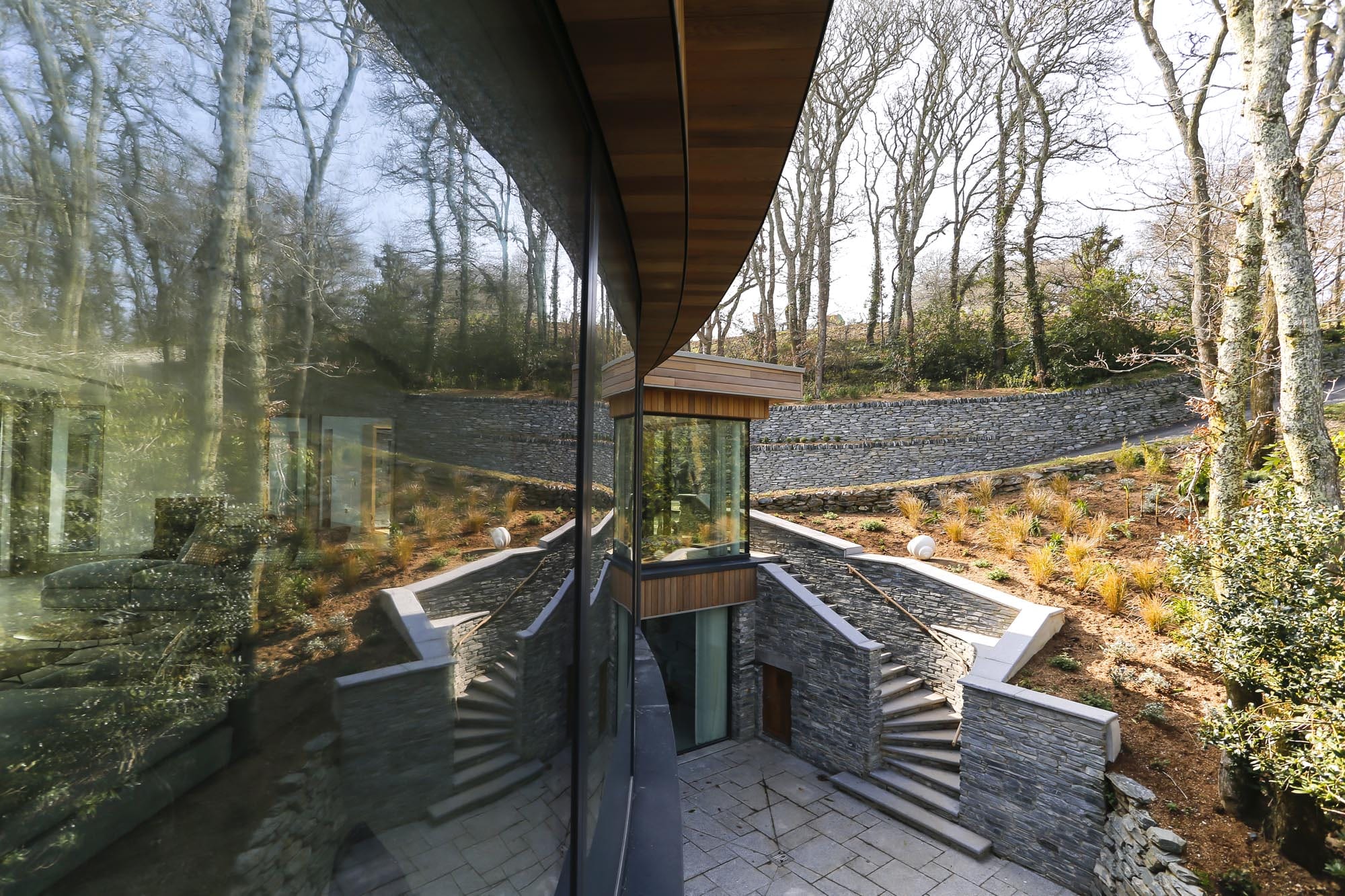 Side view of large curved window with reflection of garden and grey stonework