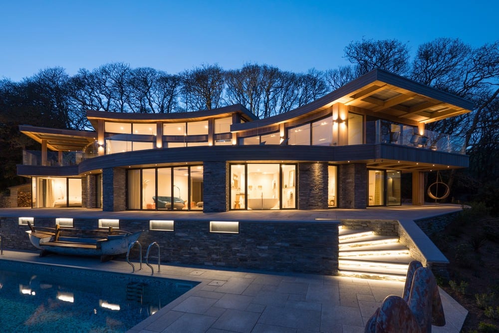House at night with curve roof, large glass windows and swimming pool.